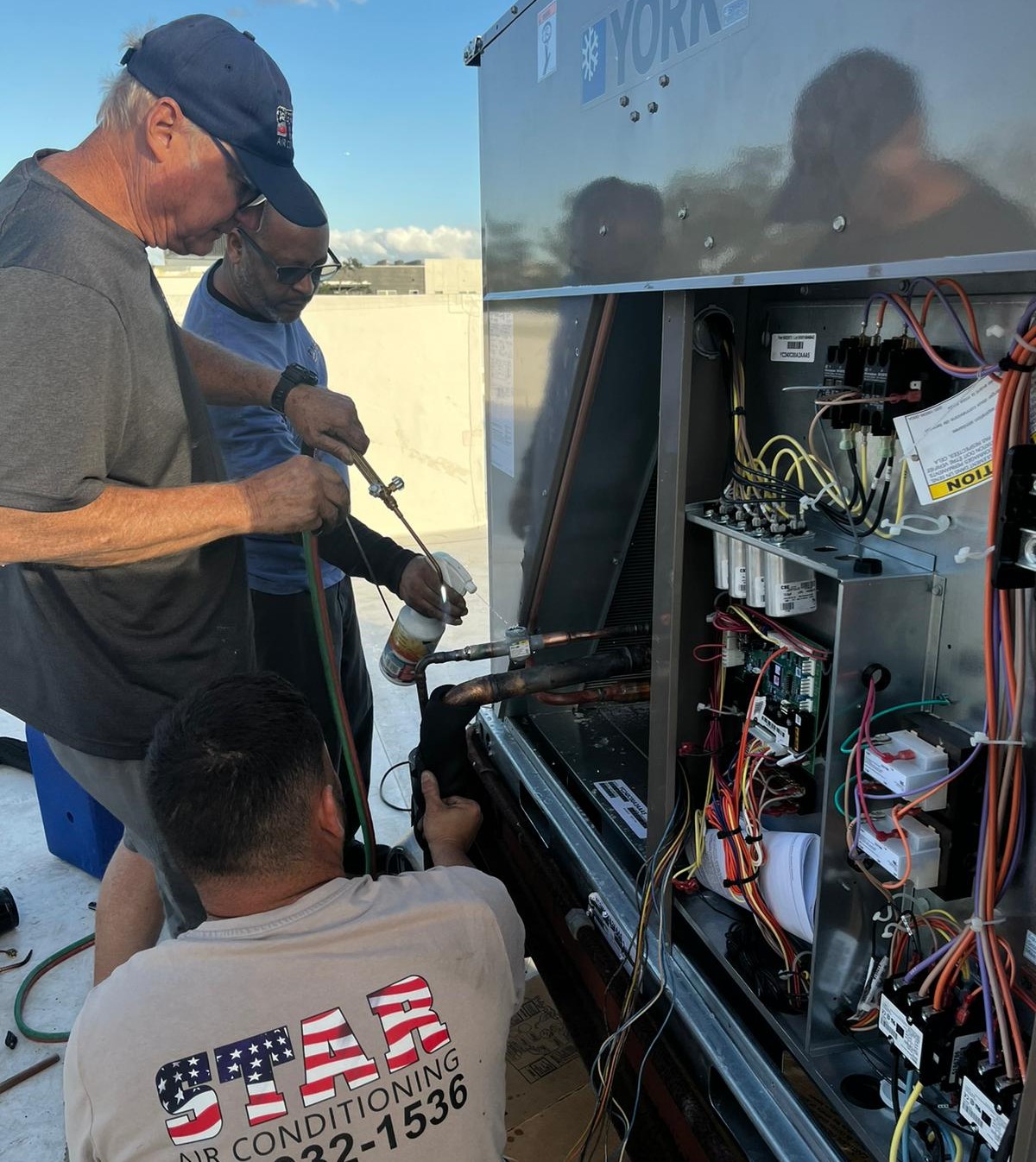 Tres hombres operando en una unidad de aire acondicionado comercial